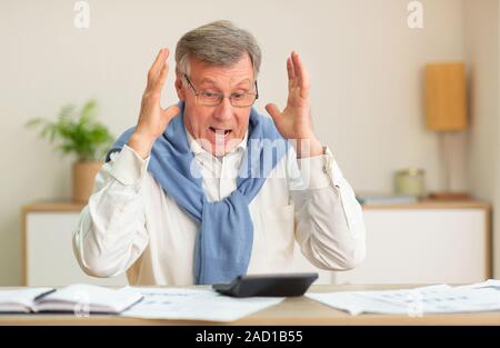 Shocked Senior Businessman Looking At Calculator Sitting In Office Stock Photo