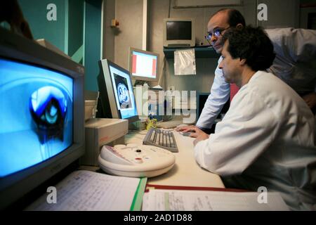 Advanced cancer treatment. Surgeons looking at a computed tomography (CT) scan while operating on a patient (in scanner on screen at left). They are u Stock Photo