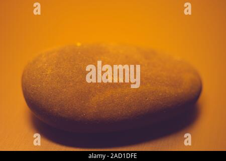 One big pebble stone on the table, orange light. Stock Photo