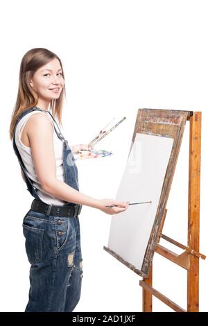 Young smiling woman painter with paintbrush standing at easel Stock Photo