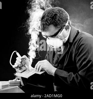 Protection from soldering fumes. Worker wearing a breathing apparatus that is protecting him from the fumes produced when soldering. He is using a sol Stock Photo