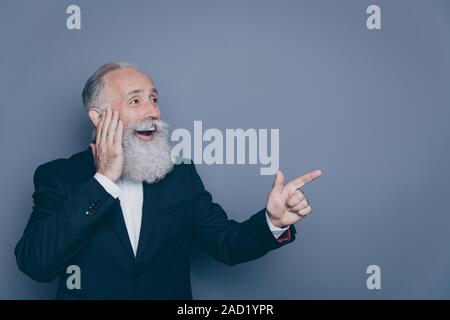 Close-up portrait of his he nice attractive cheerful cheery amazed astonished gray-haired man pointing forefinger aside copy space isolated, over grey Stock Photo