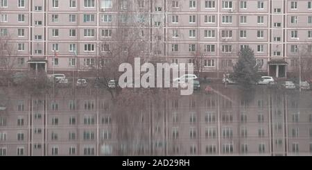 Many windows on apartment house in small town with reflection. Gray dull background. Local lifestyle and architecture Stock Photo