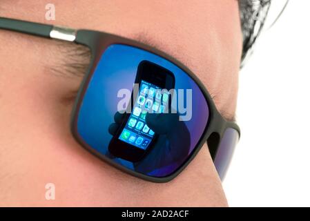 Smartphone use. Reflection in mirrored sunglasses showing a hand holding a smartphone displaying start-up icons for several mobile apps. Mobile apps a Stock Photo