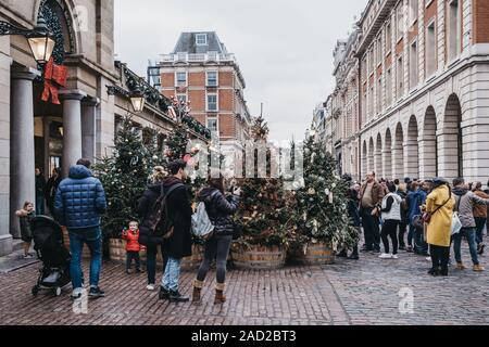 London, UK - November 24, 2019: People walking past and taking photos of  Christmas trees in Covent Garden Market, one of the most popular tourist sit Stock Photo