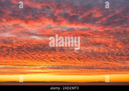 Fiery orange sunrise, sunset sky with dramatic mackerel cloud formation over the sea. Stock Photo