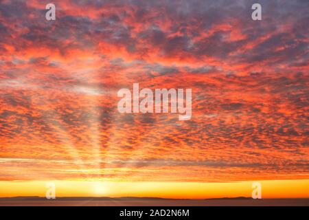 Fiery orange sunrise, sunset sky with dramatic mackerel cloud formation over the sea, sun and sun rays. Stock Photo