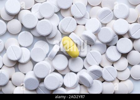 Pile of white pills and around a yellow one. The concept of different, alternative or placebo treatment Stock Photo