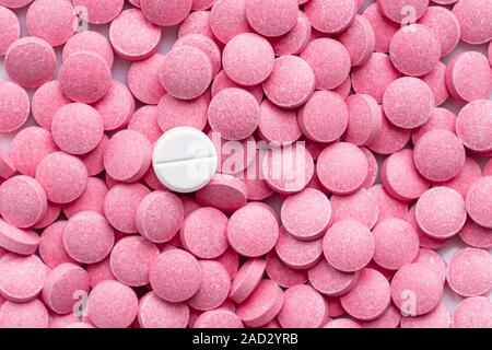 Pile of pink pills and around a white one. Medication, self-treatment or placebo concept: one tablet is different from the lot of others Stock Photo