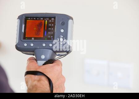 A technician uses a thermal imaging camera to check heat loss around light switches in a house. Stock Photo