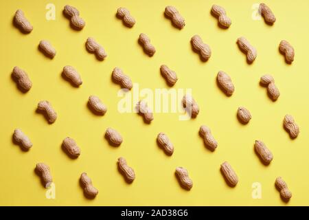 rows of peanuts in shells arranged on yellow paper background - flat lay design