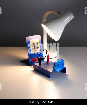 Solar cell. A table lamp shining on a pair of solar cells, generating electricity to power a small fan. Solar, or photovoltaic, cells convert light in Stock Photo