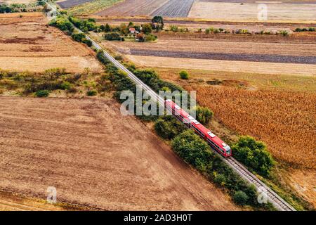 Red passenger train traveling through countryside, aerial view from drone pov in autumn afternoon Stock Photo