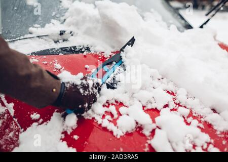 Car cleaning from snow using broom. Man taking care of automobile bumper removing ice with brush outdoors Stock Photo