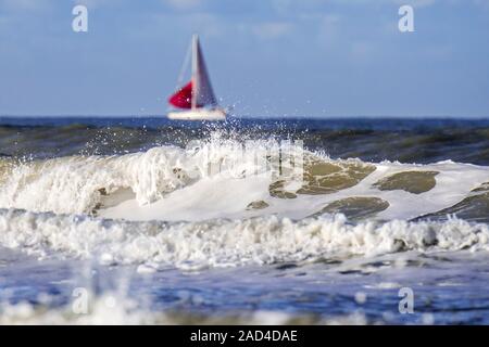 Wave breaking on the beach and sailing boat / sailboat with red sail at sea Stock Photo