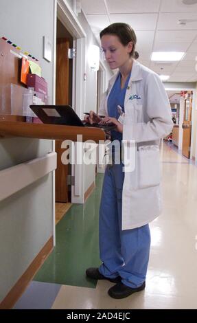 Surgeon using laptop. Surgeon working on her laptop computer outside a patient's room in a hospital. Stock Photo