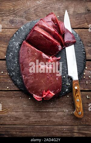 Raw liver on slate board on wooden background top view Stock Photo
