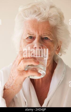 Elderly woman drinking water. Smiling 81-year-old woman drinking from a glass of water. Stock Photo