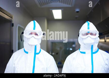 Drug manufacturing protective clothing. Two laboratory workers encased in hoods, goggles and face masks, part of protective all-body suits designed to Stock Photo