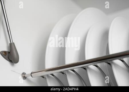 Dish drying metal rack with big nice white clean plates. Traditional comfortable kitchen. Open white dish draining closet with wet dishes of glass and Stock Photo