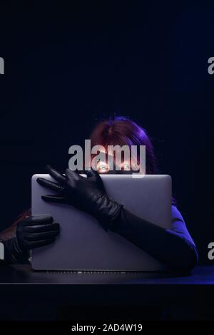 Hacker in mask holds laptop Stock Photo