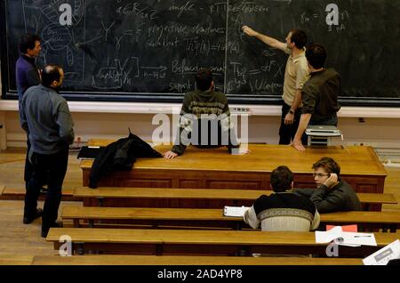 Mathematics education. University students discuss mathematical equations written on a blackboard. Stock Photo