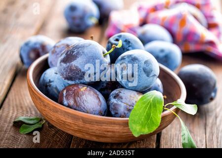 Fresh plums with green leaves on wooden rustic background Stock Photo