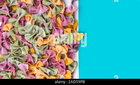 Pile of Italian dried Tri Color Farfalle pasta. Various colors of bow tie on blue color background Stock Photo