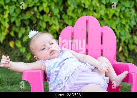 Baby Girl attempting to sit in chair outdoors, leaning over Stock Photo
