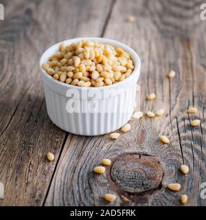 Side view of white cups, bowls with a handful of pine nut, cedar nuts on a wooden background Stock Photo