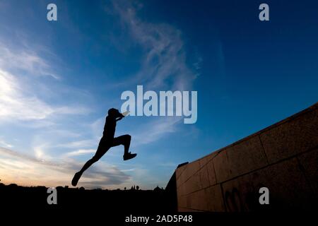 Young man practicing parkour in the street with a blue sky and backlight Stock Photo