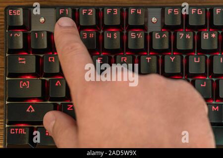 male hand presses F1 on a black keyboard with red backlight Stock Photo