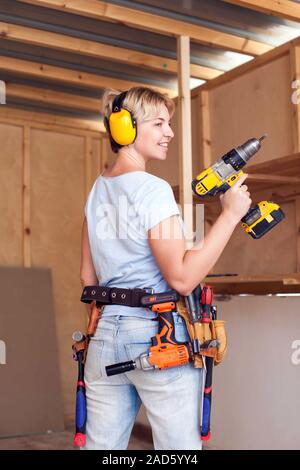 Handy woman with short hair with headphones working with drill. Stock Photo