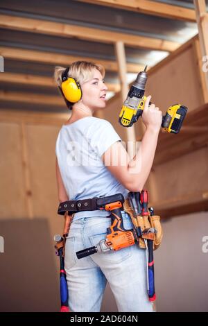 Handy woman with short hair with headphones working with drill. Stock Photo