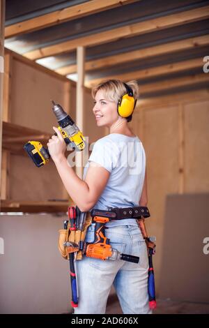 Handy woman with short hair with headphones working with drill. Stock Photo