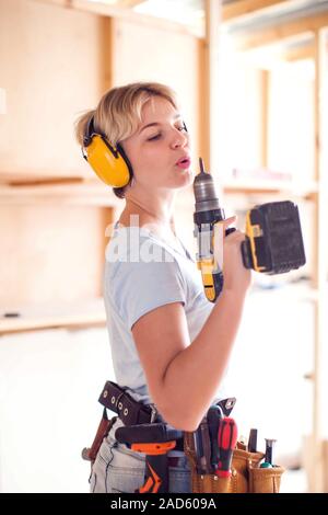 Handy woman with short hair with headphones working with drill. Stock Photo