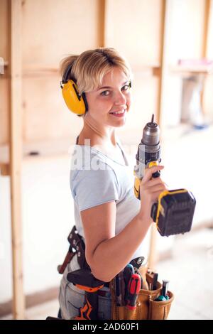 Handy woman with short hair with headphones working with drill. Stock Photo