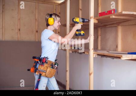 Handy woman with short hair with headphones working with drill. Stock Photo