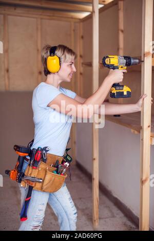 Handy woman with short hair with headphones working with drill. Stock Photo