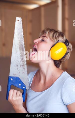 Handy woman with short hair with headphones works with saw, try to licks it. Stock Photo