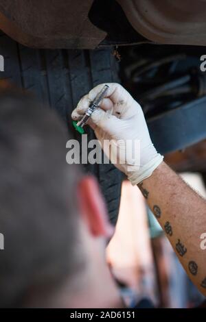 Car servicing. Technician checking the tread depth of a car's tyres with a tyre depth gauge during servicing at a vehicle service centre. Stock Photo