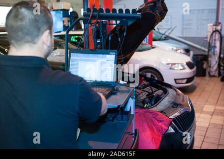 Car servicing. Technician performing an auto diagnostics check on a car being serviced in a service centre. Stock Photo