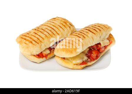 Two red onion, tomato and melted Emmental cheese paninis on a plate isolated against white Stock Photo