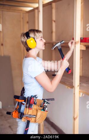 Handy woman with short hair with headphones working with hammer. Stock Photo