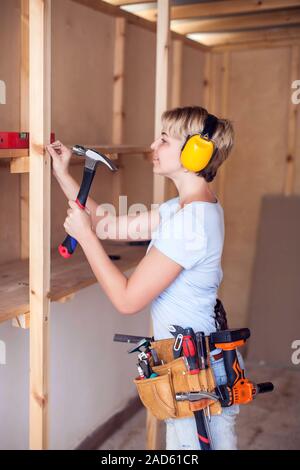 Handy woman with short hair with headphones working with hammer. Stock Photo