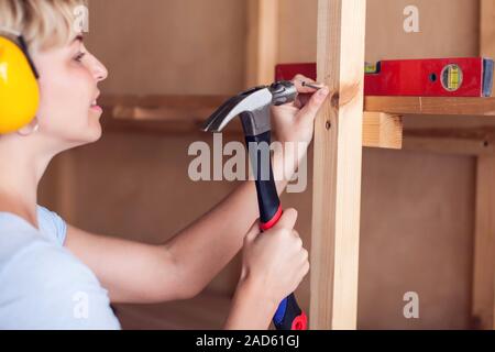 Handy woman with short hair with headphones working with hammer. Stock Photo