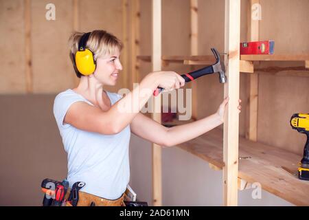 Handy woman with short hair with headphones working with hammer. Stock Photo