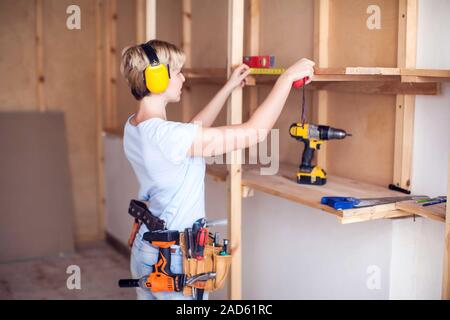 Handy woman with short hair with headphones working with building tape. Stock Photo