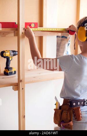 Handy woman with short hair with headphones working with building tape. Stock Photo