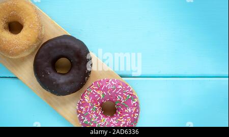Three different donuts, chocolate donut, pink icing and without icing on a wooden cutting board on a wooden blue background Stock Photo
